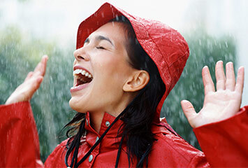 Lachende frau im Regen mit rotem Regenhut & -mantel