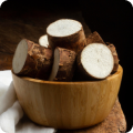 Eine Holzschale mit geschnittenen Yamswurzelstückchen steht auf einem Holztisch.
